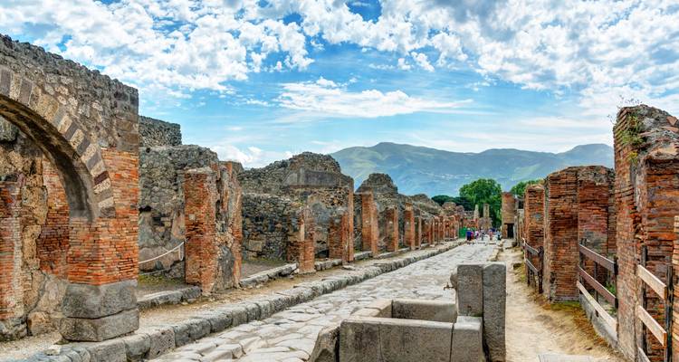 Gerade römische Straße, gesäumt von Ziegelruinen in der antiken Stadt Pompeji unter blauem Himmel.