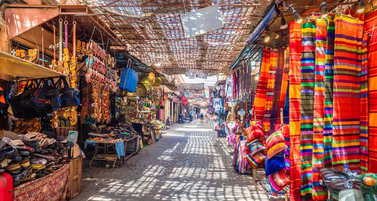 Vibrant souk alley in Marrakech lined with colourful textiles, leather goods and lanterns.
