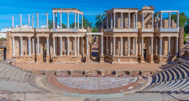 Well-preserved Roman theatre with grand colonnades and tiered seating set against a bright blue sky.
