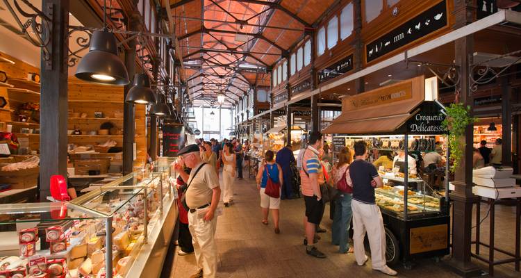 Interior de un mercado bullicioso con varios puestos de comida y gente comprando.