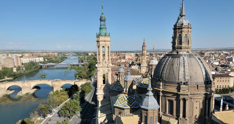 Vista aérea de una catedral con un río y puentes al fondo.