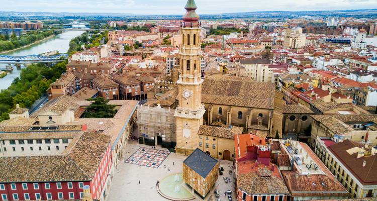 Vista aérea de una plaza del pueblo con una torre de iglesia histórica y río.