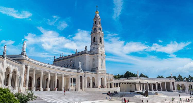 Grand Basilica of Our Lady of Fátima towers over vast white esplanade under vibrant blue sky.