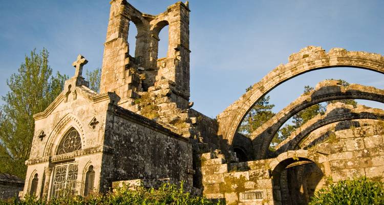 Weathered stone ruins of an ancient monastery framed by trees and evening sunlight.