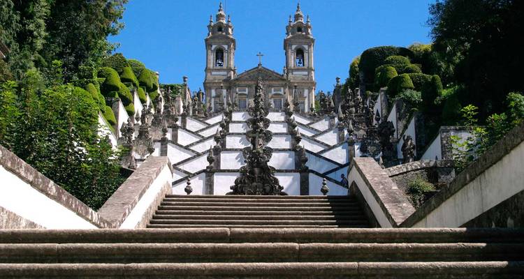 Baroque staircase of Bom Jesus do Monte ascends toward twin-towered church amid greenery.