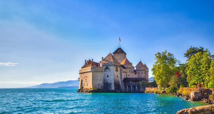 Chillon Castle stands guard over the turquoise waters of Lake Geneva beneath a clear sky.