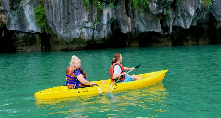 Two people kayaking near rocky cliffs.