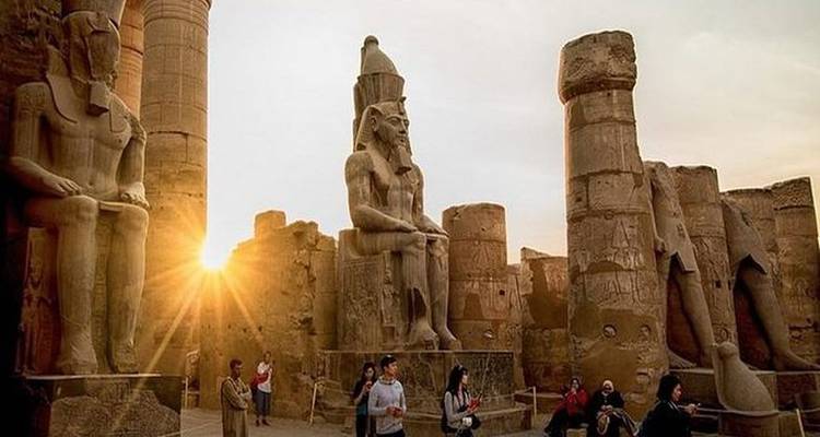 Des touristes explorant des ruines anciennes avec des statues sculptées au coucher du soleil.