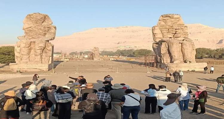 Groupe de touristes sur un site antique avec de grandes statues et des colonnes.