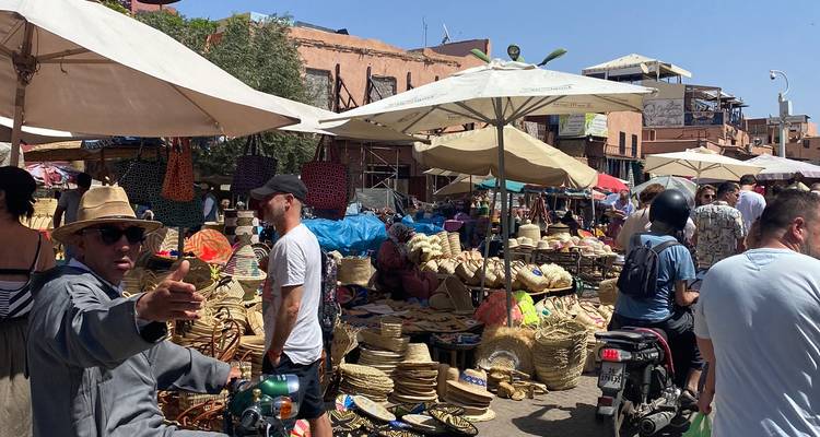 Drukke buitenmarkt in Marrakesh met verkopers, geweven manden, scooters en zonnetenten.