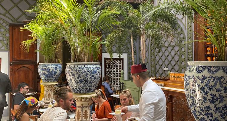 Elegant restaurantinterieur met sierlijke zuilen, palmen en een ober in traditionele fez die gasten bedient.