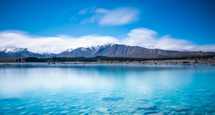 Glass-smooth turquoise water of Lake Tekapo with snowy peaks under a clear blue sky.