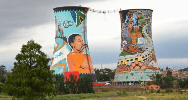 Zwei hoch aufragende Soweto-Kühltürme, bemalt mit lebendigen Gemeinschaftswandmalereien unter grauem Himmel.