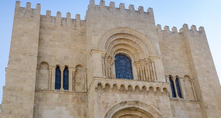 Steinfassade der Alten Kathedrale von Coimbra mit gewölbtem Türeingang und kleinen gotischen Fenstern.