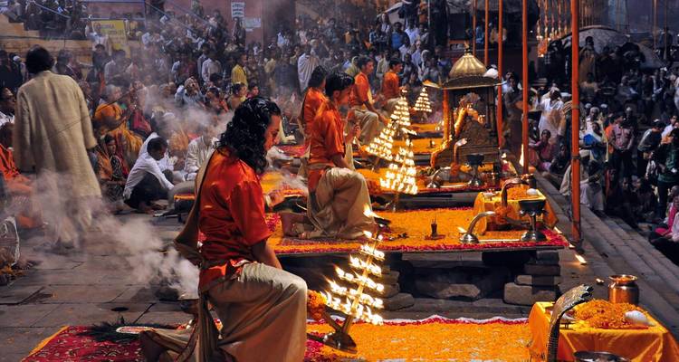 Zeremonielle Veranstaltung mit Menschen, die Rituale am Fluss durchführen und brennende Lampen halten.