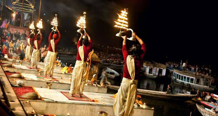 Menschen, die am Ufer eines Flusses das abendliche Aarti durchführen.