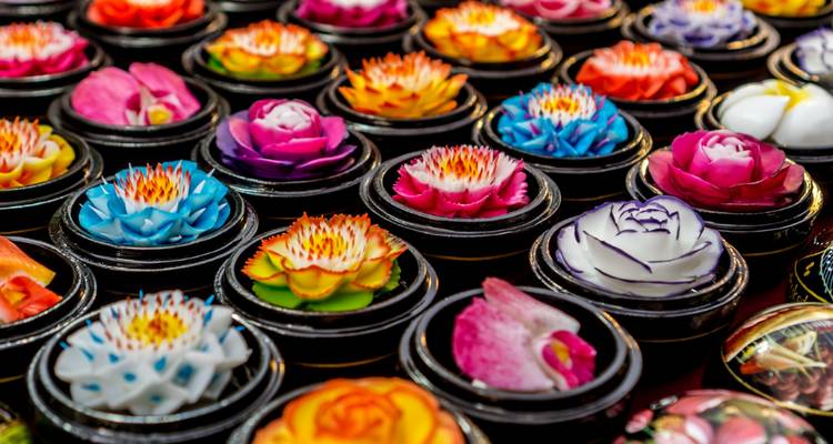 Filas de flores de jabón talladas en colores brillantes exhibidas en pequeños recipientes.
