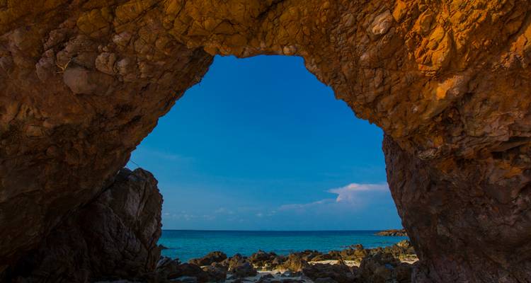 Un arco natural de mar enmarca un océano azul vibrante y una costa rocosa.