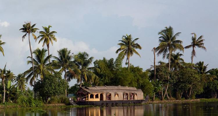 Une péniche traditionnelle flottant sur un bras mort calme avec des palmiers.