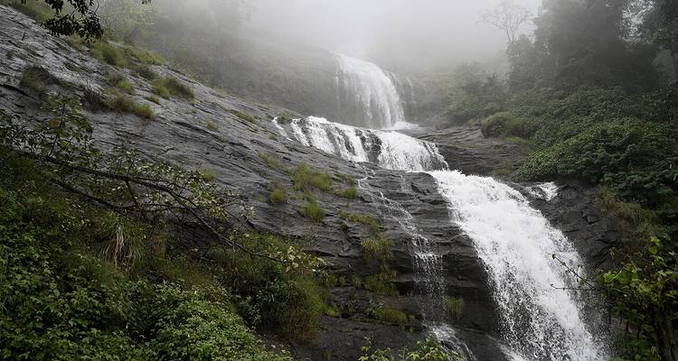 Une cascade qui tombe en cascade sur des rochers entourée de brume.
