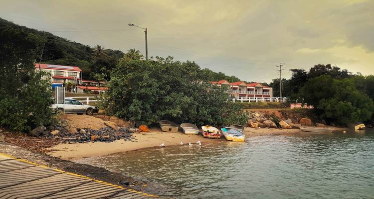 Pequeño pueblo costero con botes amarrados, manglares y luz tenue del atardecer bajo un cielo encapotado.
