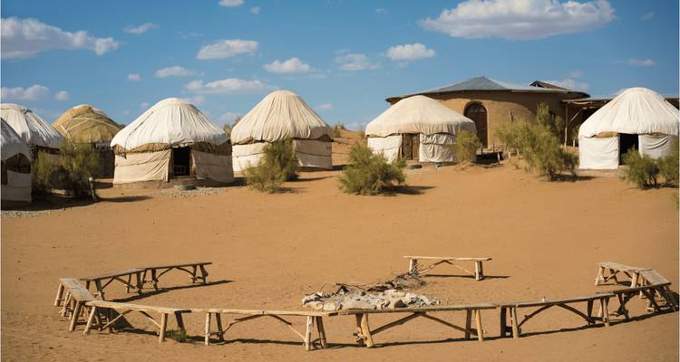 Camp de yourtes traditionnel dans un décor désertique sous un ciel bleu.