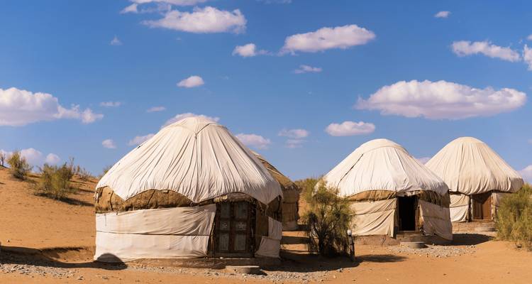Trois yourtes traditionnelles dans un paysage désertique sous un ciel dégagé.