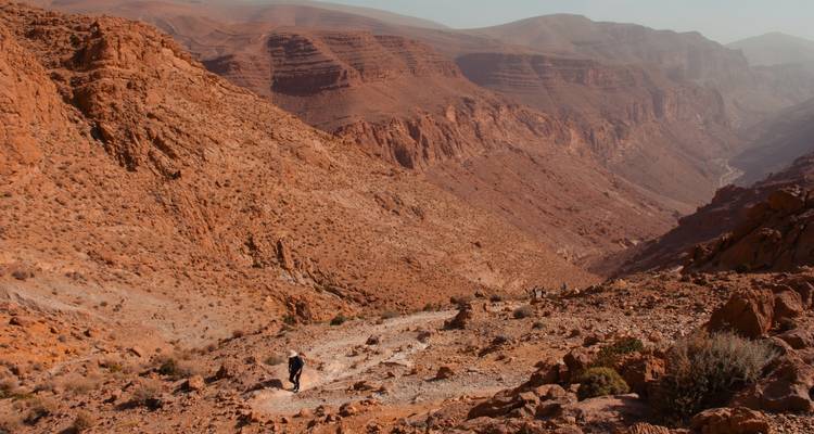 Hikers making their way along a rocky trail in the deep red canyon landscape of Dades Gorge.