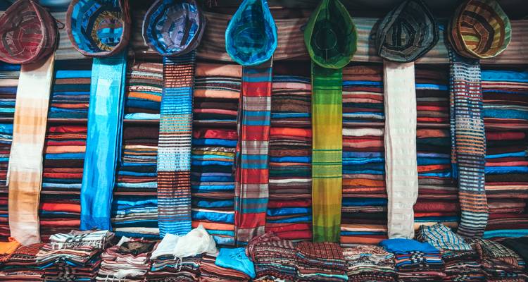 Stacks of vibrant woven scarves hanging and folded in a Moroccan market stall.