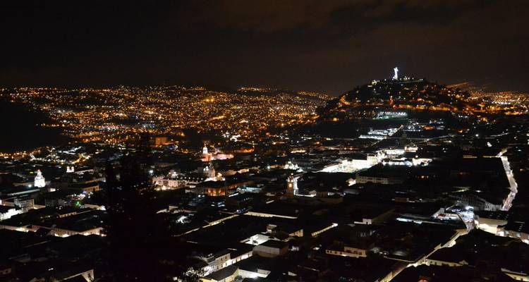 Paisaje nocturno de Quito con casas iluminadas y una estatua en la cima de una colina