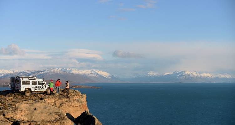 Un véhicule garé sur une falaise surplombant un lac et des montagnes au loin.
