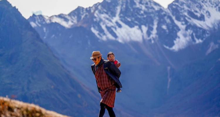 Mann trägt ein Kind in bergigem Gelände