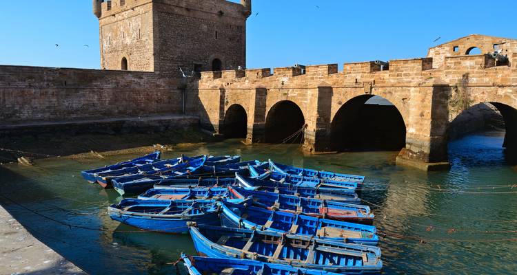 Cluster of blue boats near a stone bridge in Essaouira.
