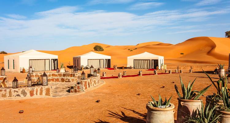 Campamento de lujo en el desierto con tiendas blancas y dunas de arena.
