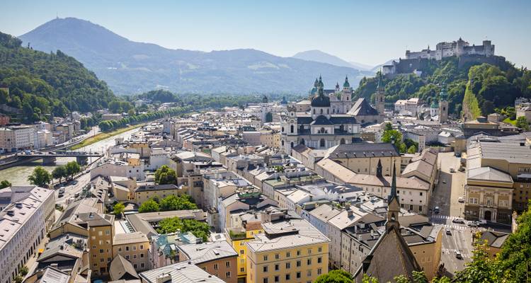 Panoramic aerial view of Salzburg with the fortress on the hill, cathedral domes, and the Salzach River.