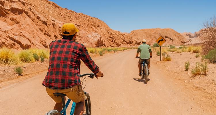 Deux cyclistes sur une route désertique avec des montagnes arides en arrière-plan.