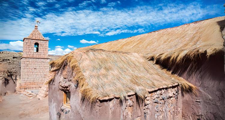 Église traditionnelle en pierre avec toit de chaume sous un ciel bleu vibrant.