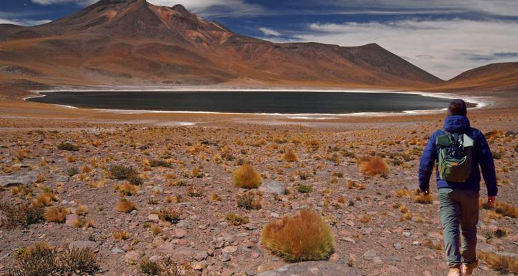 Personne marchant vers un lac d'altitude entouré de montagnes.
