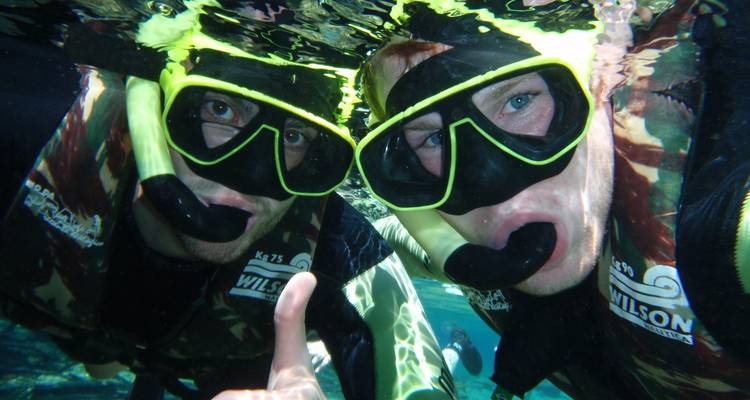 Twee snorkelaars poseren onder water met neon maskers in kristalhelder water.