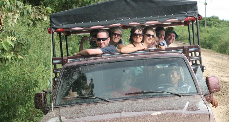 Groep reizigers rijdt in een open modderige safaritruck langs een junglepad.