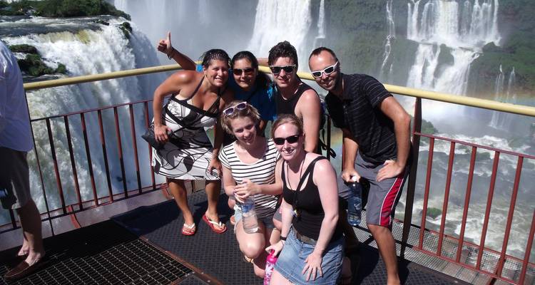 Vrienden poseren op een uitkijkplatform met de donderende Iguazu-watervallen achter hen.
