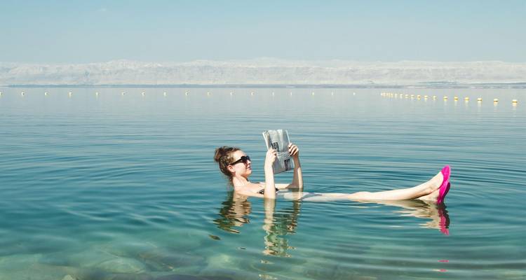 Woman leisurely floats on her back reading a newspaper in the calm, clear waters of a vast salt lake.