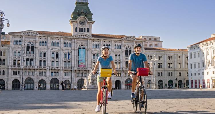 Ciclistas frente a un gran edificio histórico en una plaza de la ciudad.