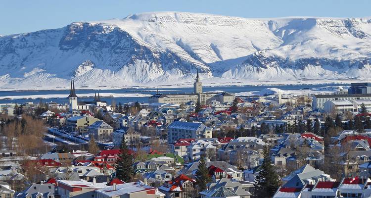 Winter panorama of Reykjavik’s colorful rooftops with snow-covered Mount Esja towering behind.