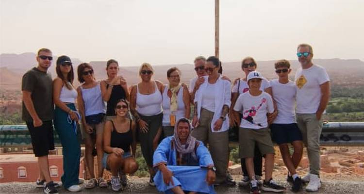 Un groupe de touristes pose à un point de vue en bordure de route avec une vallée désertique brumeuse s'étendant derrière eux.