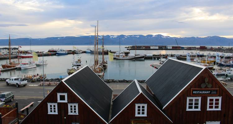 Quaint harbour scene with wooden-roofed buildings and snow-flecked mountains across the fjord in Húsavík.