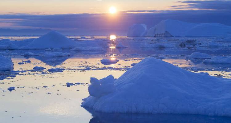 Polar landscape with icebergs and a setting sun reflecting on the water.