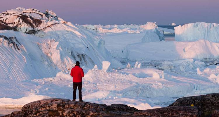 Person standing on a rocky platform overlooking an icy landscape.