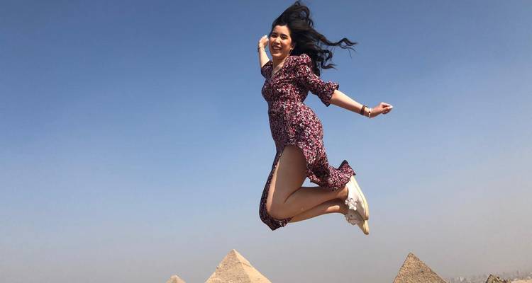 Mujer saltando con pirámides en el fondo.