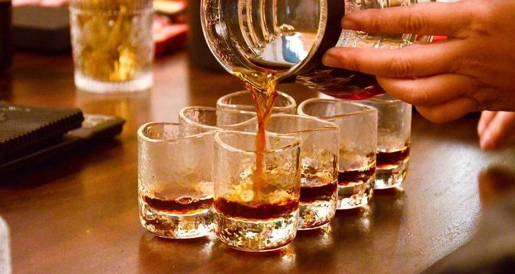 Primer plano de café rico vertiéndose en una fila de pequeños vasos de degustación
